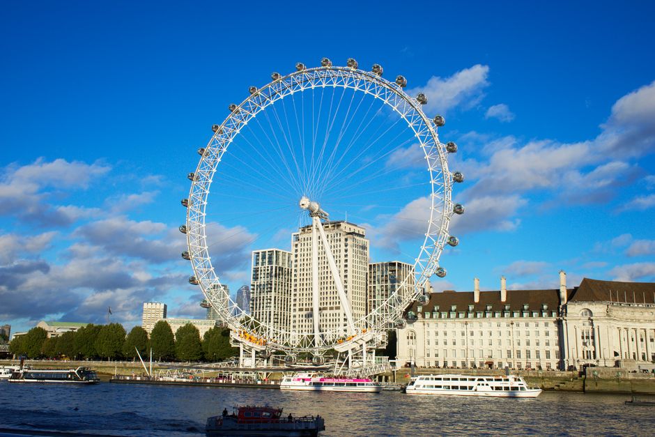 A spacious, well-maintained park with a lush, green lawn and a circular bandstand structure with a dark, domed roof and white support columns situated centrally. The grassy area is evenly trimmed with